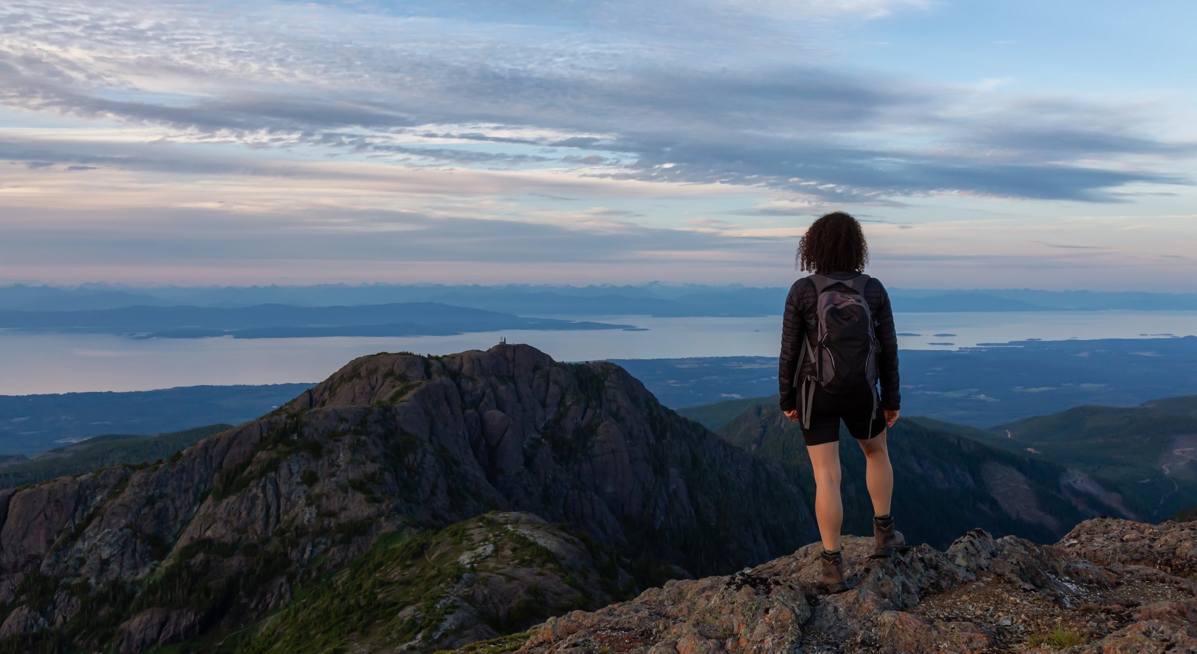 femme de dos portant une veste Vertical Sports faisant une randonnée dans les montagne. 